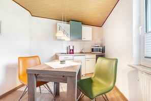 Une cuisine compacte avec une table en bois, deux chaises, un four à micro-ondes et une machine à café.