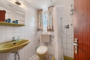 Un bagno con lavandino, wc, doccia e una finestra con tende.