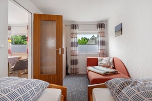 Una camera da letto con due letti, una porta in legno, una finestra con tende, un tavolino e un divano.
