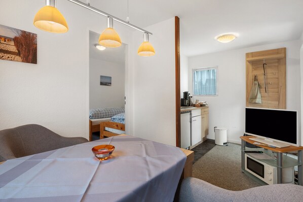 A compact hotel room with a bed, a dining table, a kitchenette, and a TV. - Small Holiday Home in Cuxhaven (Cuxhaven)