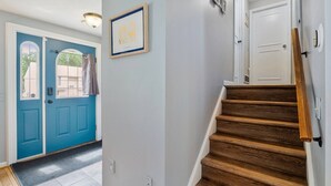 A hallway with a blue door, a framed picture on the wall, and a wooden staircase.