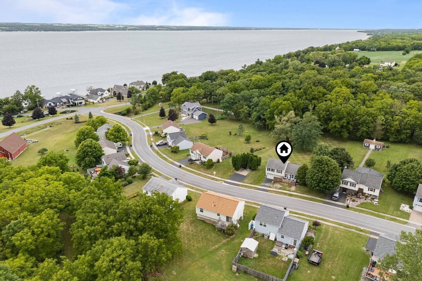An aerial view of a residential area with houses, a winding road, and a body of water in the background.