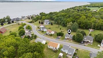 An aerial view of a residential area with houses, a winding road, and a body of water in the background.