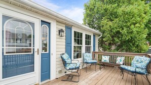 A covered porch with a wooden deck, a blue door, and two rocking chairs with patterned cushions.