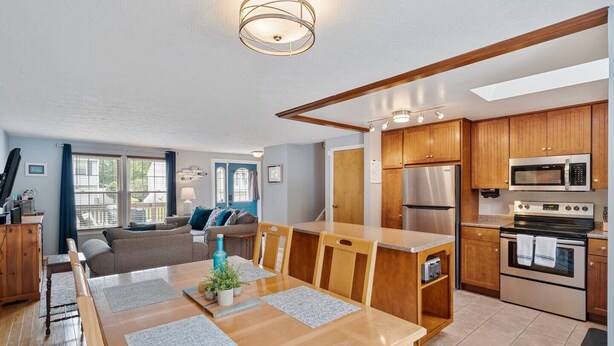 A modern kitchen with wooden cabinets, stainless steel appliances, and a dining area with a wooden table and chairs.