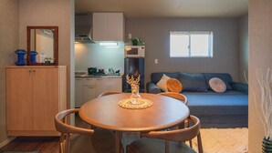 A compact living space with a dining area, kitchenette, and a sofa in the background. - New open F Maison Kishinosato 301 (Osaka)