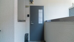A narrow hallway with a grey door, a small trash bin, and a wall-mounted electrical box. - New open F Maison Kishinosato 301 (Osaka)