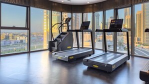 A gym with treadmills and a stair climber, large windows with a city view, and a modern interior design. - KeyRock Living - Skyline at Paramount (Dubai)