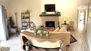 A living room with a fireplace, a television mounted above it, and a wooden coffee table with plants. - 2 BR Jiminy Peak w Mountain View Sleeps 7 Gorgeous (Hancock)