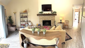 A living room with a fireplace, a television mounted above it, and a wooden coffee table with plants.