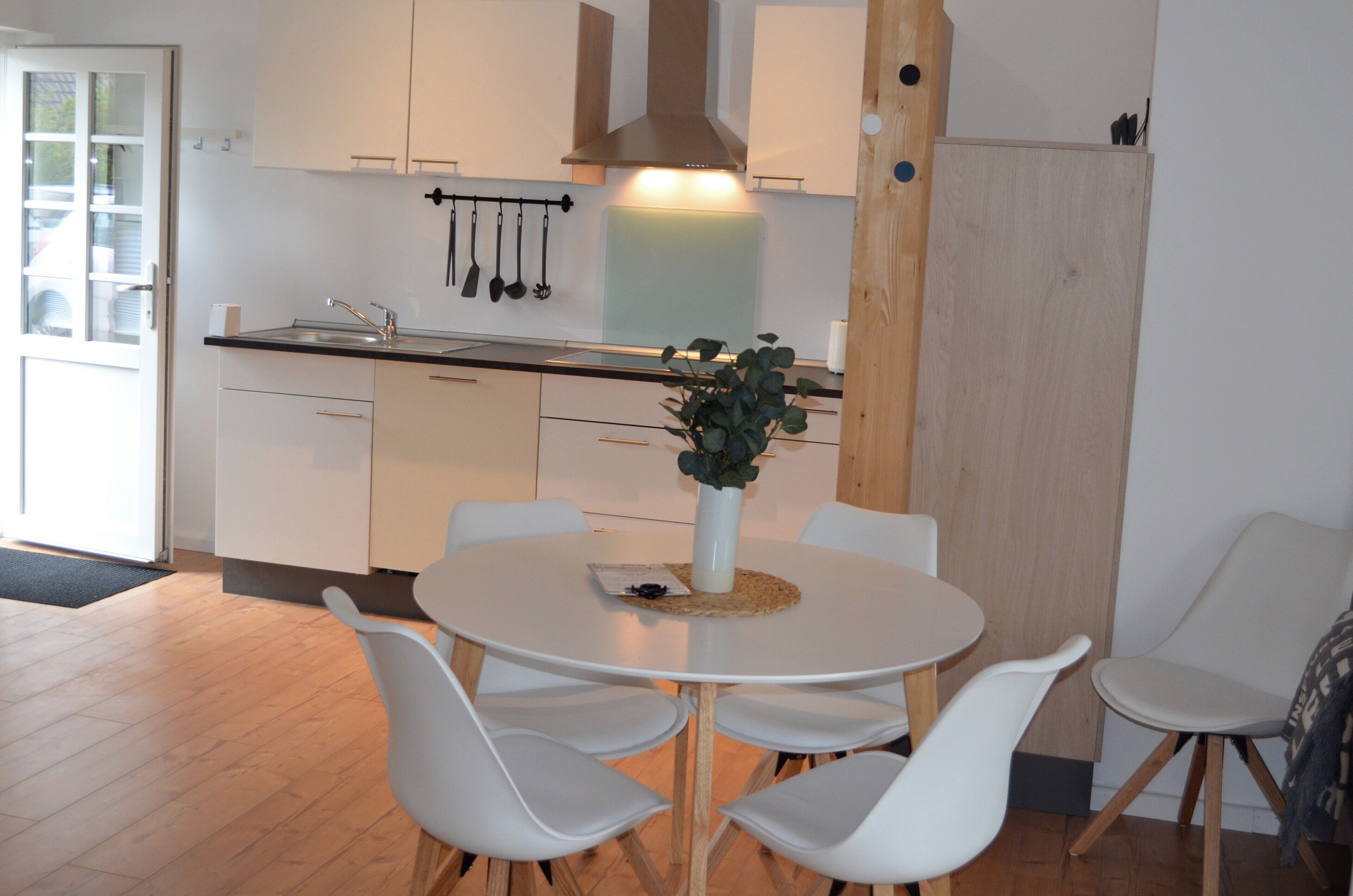 A modern kitchen with white cabinets, a central island with chairs, a hanging pot rack, and a wooden door.
