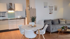 A modern kitchen with white cabinets, a round dining table with white chairs, and a grey sofa in a living area.