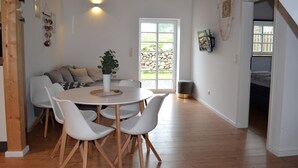 A dining area with a round table, white chairs, a sofa, and a potted plant.