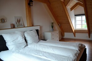 A bedroom with a bed, a nightstand, a dresser, a window, and a wooden ceiling.