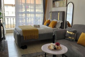 Un dormitorio moderno con cama, sofá, mesa redonda y un amplio ventanal.