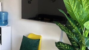 A room with a yellow chair, a green pillow, a water dispenser, and a large green plant.