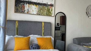 A neatly made bed with a grey headboard, white and yellow pillows, and a rolled-up towel on the bed.