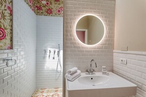 A bathroom with white subway tiles, a round mirror with a light, a sink, and a shower area. - Villa Belvedere Condor - L - with Pool (Alassio)