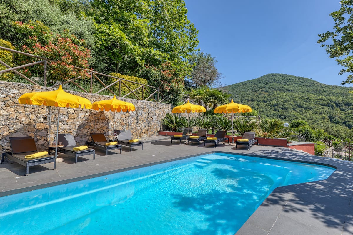 Une piscine entourée de murs de pierre et de verdure, avec des chaises longues et des parasols jaunes.