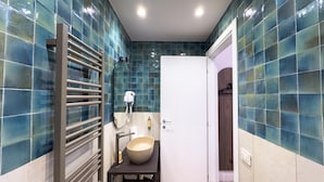 A bathroom with blue-tiled walls, a white door, a towel rack, a sink, and a shower area. - Guest House Le Sei Porte   Porta di Mare (Salerno)