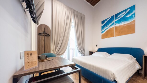 A hotel room with a bed, a desk, a chair, a window with curtains, and a painting on the wall. - Guest House Le Sei Porte   Porta di Mare (Salerno)