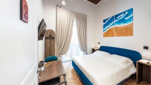 A bedroom with a large bed, a desk, a chair, a window with curtains, and a painting of waves on the wall. - Guest House Le Sei Porte   Porta di Mare (Salerno)