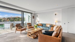 Ein geräumiges Wohnzimmer mit großem Fenster, einem blauen Sofa, zwei Ledersesseln und einem Holztisch.
