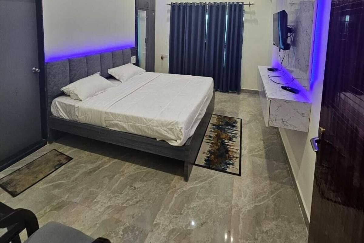 A modern bedroom with a bed, a desk with a computer, a ceiling fan, and a TV mounted on the wall.