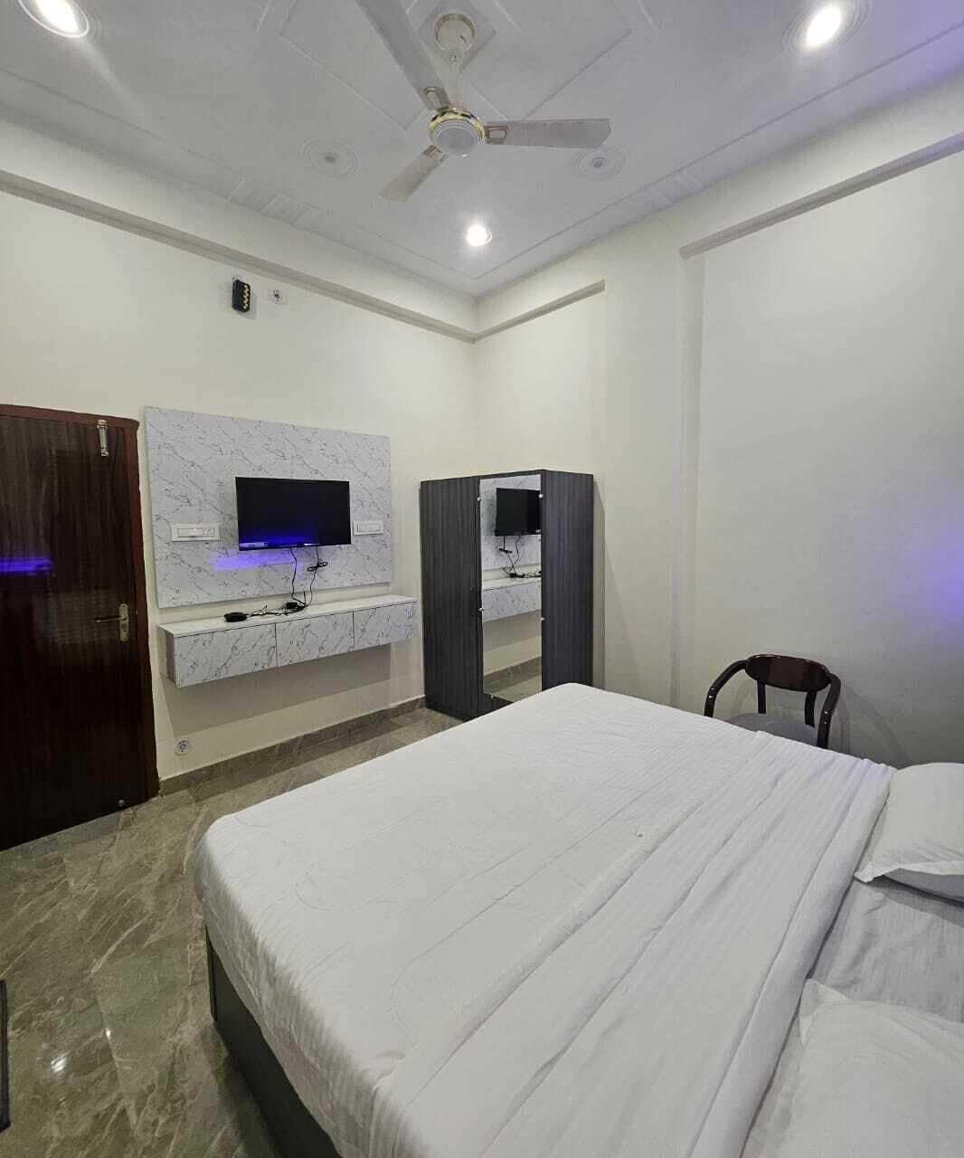 Habitación de hotel con cama, televisor montado en la pared, armario y ventilador de techo.