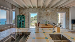 A kitchen with stone walls, a view of the sea, and a dining area with a table and chairs.