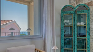 A room with a view of a building through a window, a chair, a lamp, and a teal-framed cabinet.