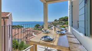 A balcony with a table set for dining, overlooking a coastal view with buildings and trees.