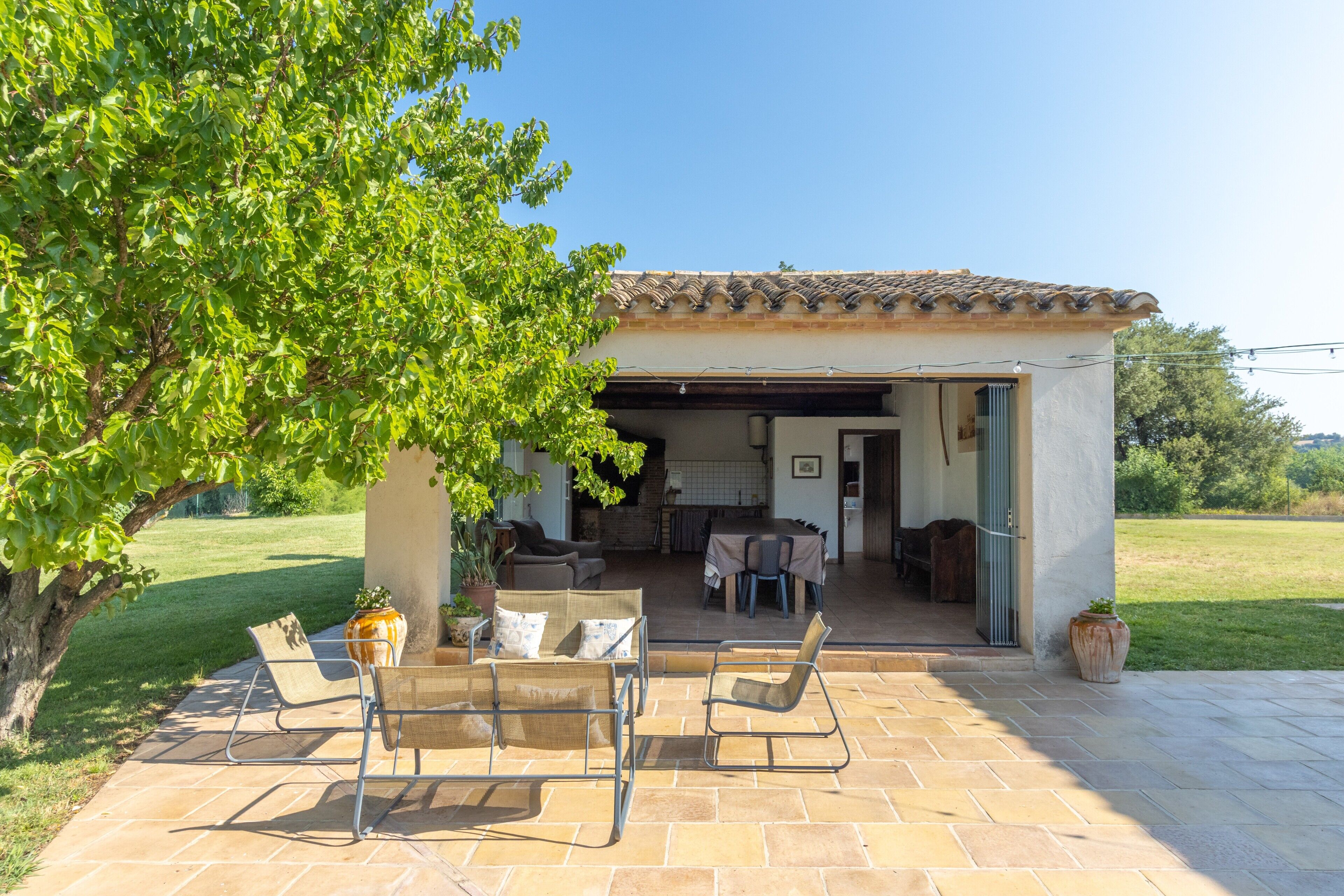 Une terrasse avec des meubles d’extérieur, un espace abrité avec une table et des chaises, et une vue sur le paysage environnant.