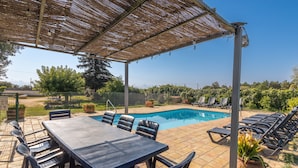 Ein überdachter Außenbereich mit Pool, Liegestühlen und Esstisch mit Stühlen.