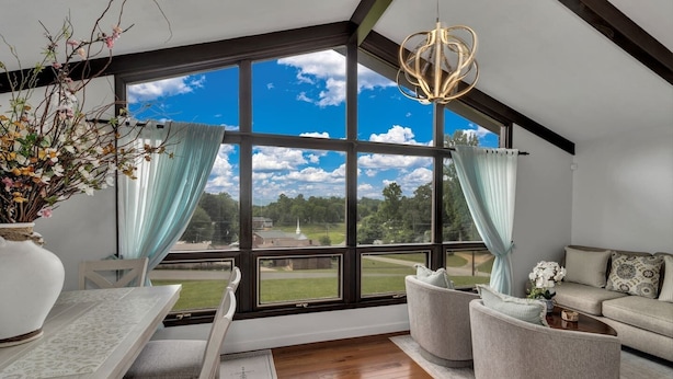 Ein geräumiges Zimmer mit großem Fenster und Blick auf einen Golfplatz, einem modernen Kronleuchter und einer gemütlichen Sitzecke mit Sofa und Sesseln.