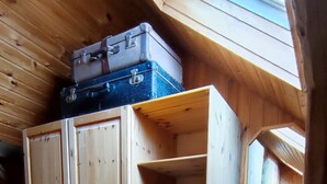 Une pièce en bois avec un plafond en pente, une armoire dotée de nombreux tiroirs, une petite table de chevet et une fenêtre.
