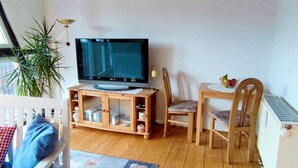 Un salon avec un téléviseur, des meubles en bois, une plante et un radiateur.