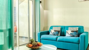 A teal sofa with patterned cushions, a glass table with a fruit bowl, and a view of a cityscape through large windows. - Comfortable apartment with terrace near Saint-Denis (La Possession)