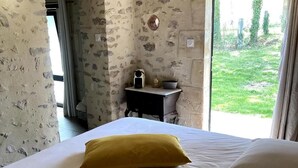 A bedroom with a bed, a yellow pillow, a small table with a speaker and a bowl, and a stone wall. - Guesthouse near La Flèche - Pets Allowed - Breakfast Included (Bazouges Cré sur Loir)