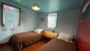Une chambre avec deux lits, un plancher en bois, un ventilateur de plafond et des fenêtres ornées de rideaux en dentelle.