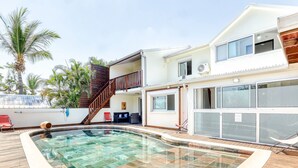 A two-story house with a swimming pool, a wooden deck, and a staircase leading to the upper floor. - Comfortable apartment with terrace and direct pool access (La Possession)