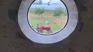 A window with a view of a red tractor in a field.