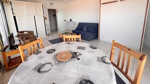 A dining area with a round table, chairs, and a central rug. There is a sofa and a radiator in the background. - Studio sea view and balcony, 10th floor (Les Sables-d'Olonne)