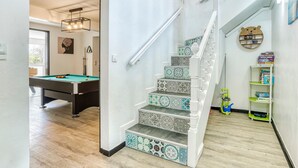 A staircase with patterned tiles, a pool table, and a bookshelf with children's books.