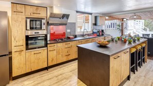 A modern kitchen with wooden cabinets, stainless steel appliances, and a large island with a fruit bowl.