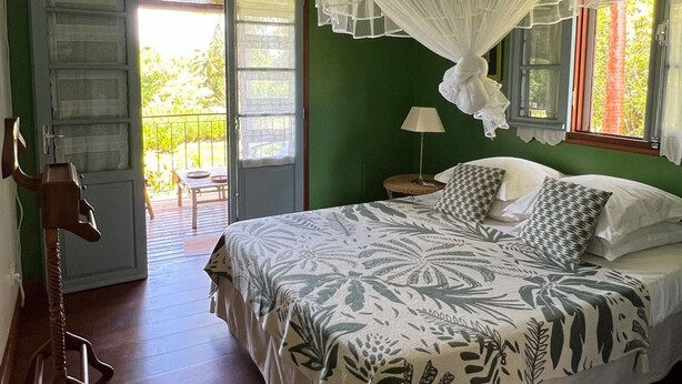 A bedroom with a bed, a nightstand, a lamp, a window with a view, and a door leading to an outdoor area.