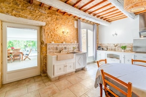 Une cuisine avec des murs en pierre, un évier, des placards et un coin repas avec des chaises.