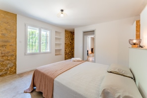 Une chambre à coucher avec un lit, un mur en pierre, une fenêtre et une porte donnant sur une autre pièce.