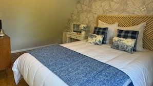 Un dormitorio con papel tapiz estampado, una cama con colcha azul y blanca, y una mesita de noche con una lámpara.