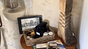 A rustic room with a stone wall, a wooden table with a basket of items, a wine glass, and travel brochures.
